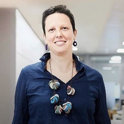 Woman in tech with dark brown hair and blue button down shirt standing at Global Relay London office.