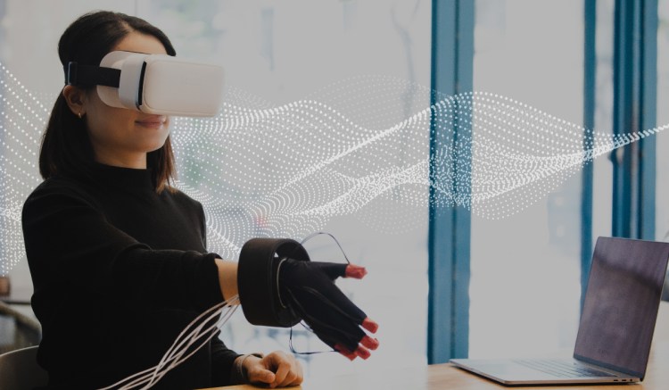 Woman sitting at desk wearing AR Goggles with hand outstretched for a handshake.