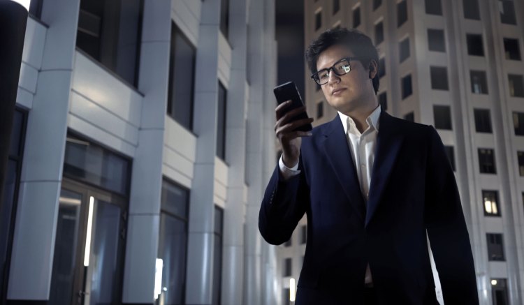A business person wearing a dark suit looks at their mobile phone, appearing concerned.