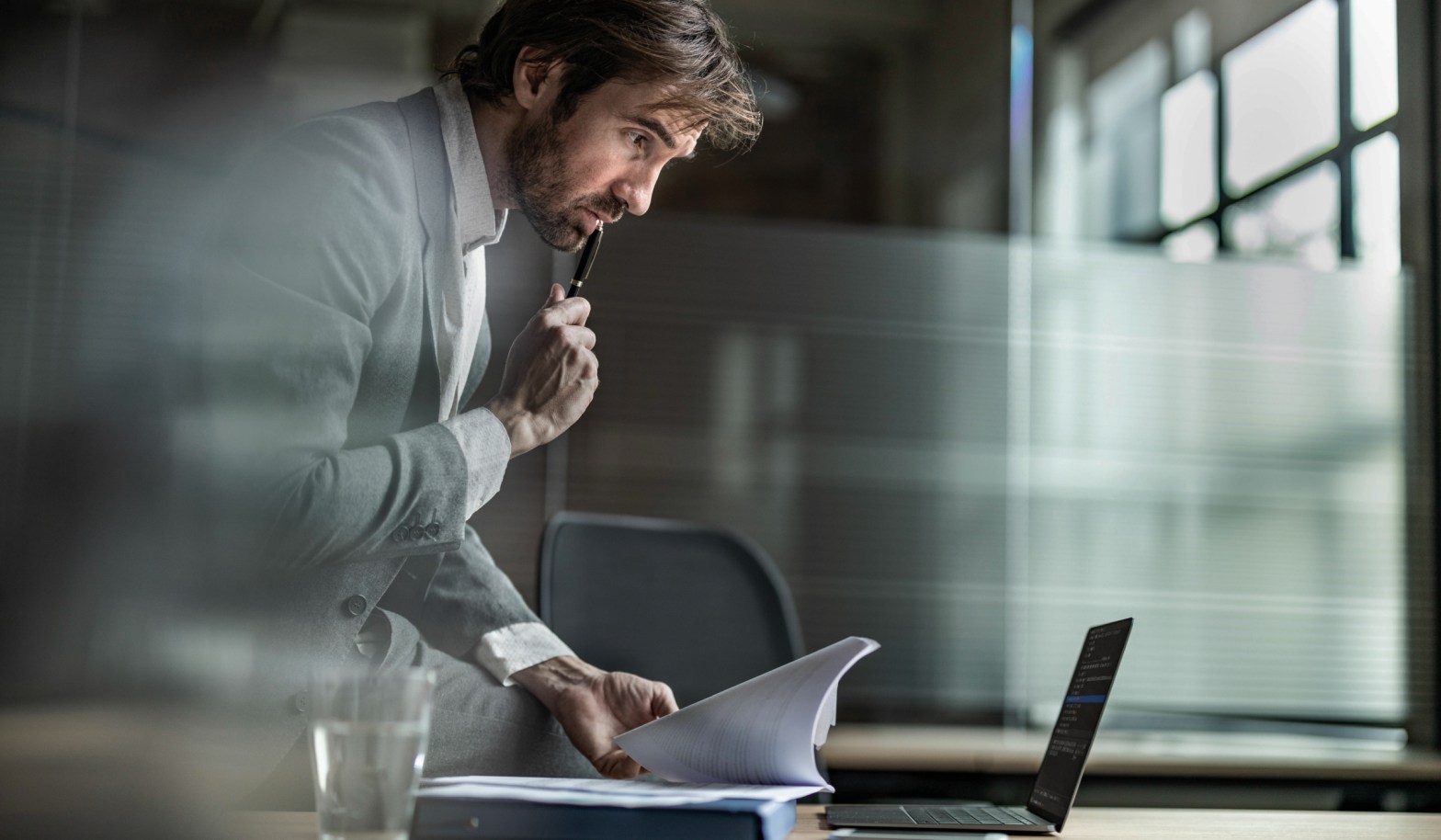 A businessman checking papers whilst looking at a laptop